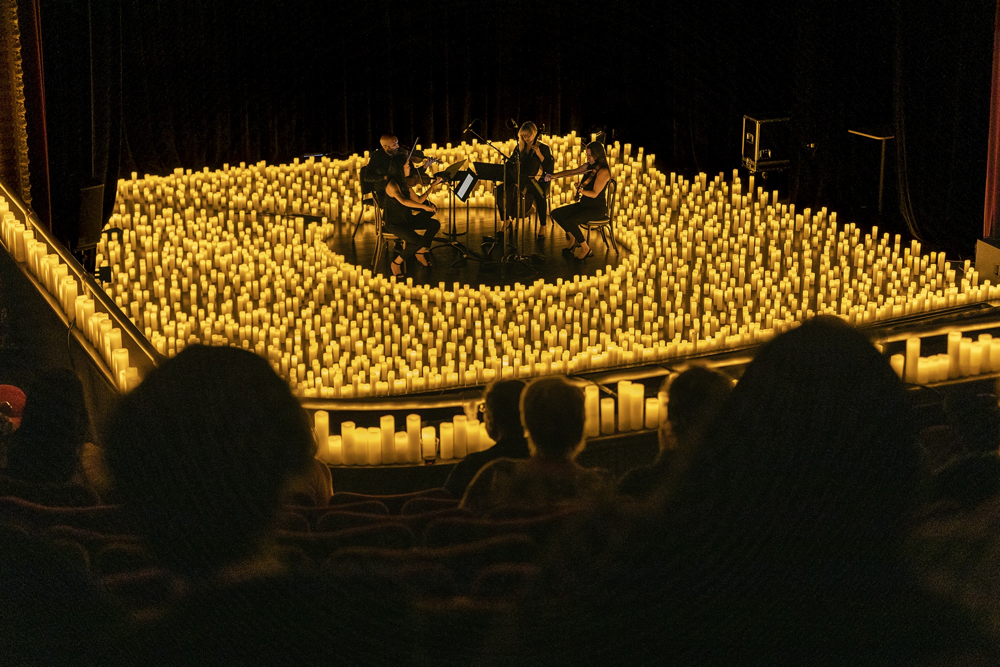 View from the audience looking across at a string quartet performing in circle surrounded by hundreds of candles. 