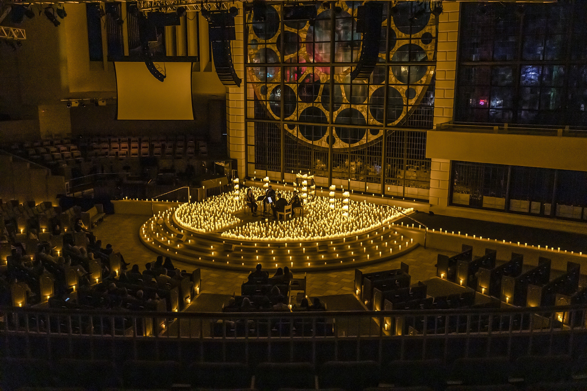 A wide shot of the interior of the First Baptist Church in St. Petersburg revealing a string quartet performing on stage surrounded by candles.